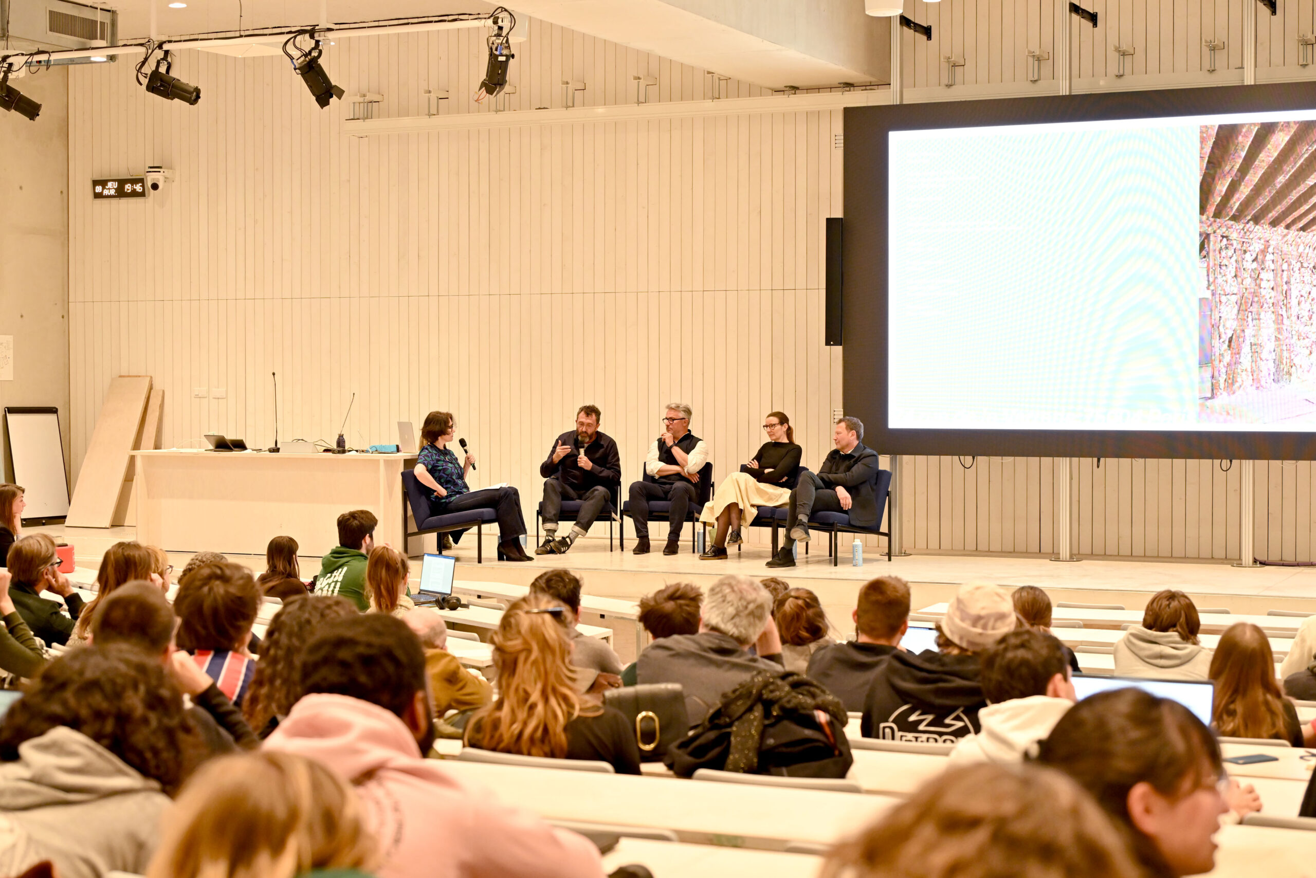 Table ronde "Confortements" réunissant cinq intervenants face à un amphithéâtre étudiants et professionnels, événement de l'agence AT